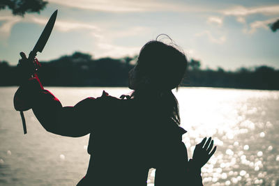 Rear view of silhouette woman standing in lake against sky