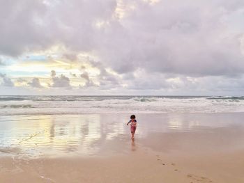 Toddler running on shore at beach against cloudy sky