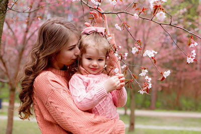 Mother and little girl in pink clothes, hugging in the park with blooming pink sakura.