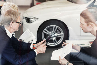 Salesman showing agreement to senior couple in car dealership