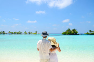 Couple in hat standing at beach against sky