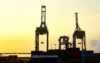 Cranes at construction site against sky during sunset