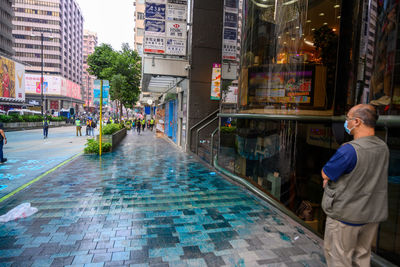 Rear view of man standing on street by buildings in city