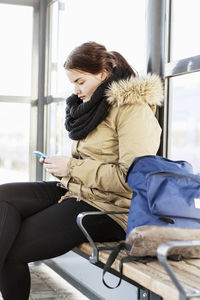 Young woman using mobile phone on bench at train station