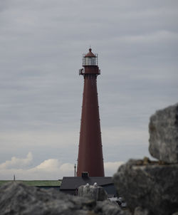Lighthouse on rock by building against sky