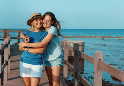 Portrait of mother and daughter embracing against sea