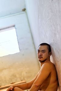 Portrait of shirtless mid adult man sitting by wall in room