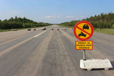 Road sign on airport runway amidst trees against sky