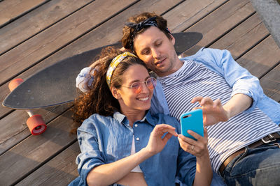 Top view of man and woman with skateboard watching video or photos on smartphone
