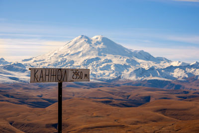 Information sign on snowcapped mountains against sky