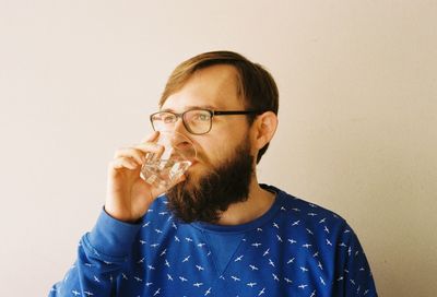 Bearded man drinking water against wall