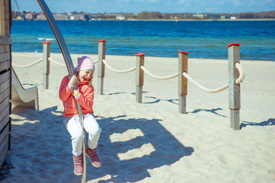 Full length of playful girl hanging on metal at beach