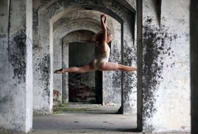 Full length of ballet dancer jumping against in abandoned building