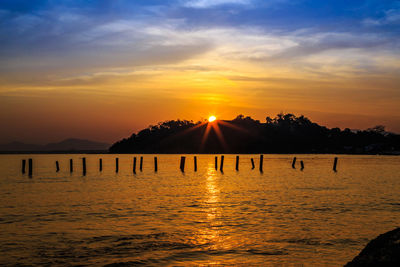 Silhouette wooden posts in sea against sky during sunset