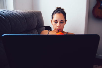 Woman using laptop while slipping drink at home