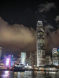 Illuminated buildings by river against sky at night