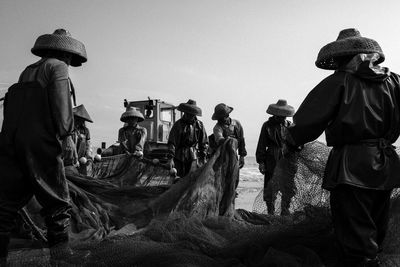 Men holding fishing net at beach against clear sky