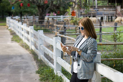 Asian woman watching tablet beside a white fence