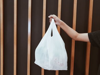 Cropped hand holding plastic bag against metal grate