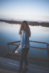 Woman standing on pier over lake against sky