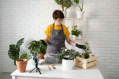 Side view of woman holding potted plant in kitchen