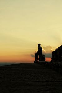 Rear view of man sitting on rock at sunset