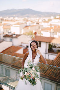 Smiling bride with bouquet standing against cityscape