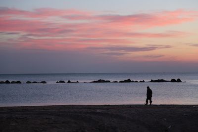 Silhouette man standing on beach against sky during sunset