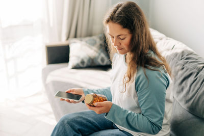 Young woman using mobile phone while lying on bed at home