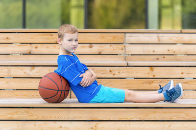 Portrait of boy sitting by basketball on seat