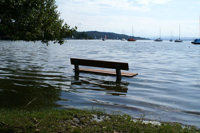 Empty bench on pier by lake against sky