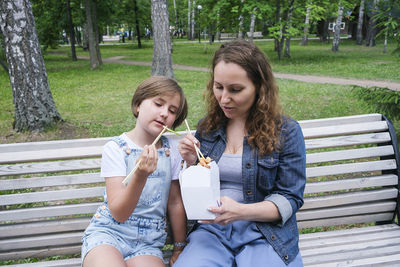 Mid adult mature woman and teenage girl on a summer day in the park has lunch with noodles wok