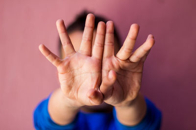 Close-up of woman gesturing stop sign against pink background