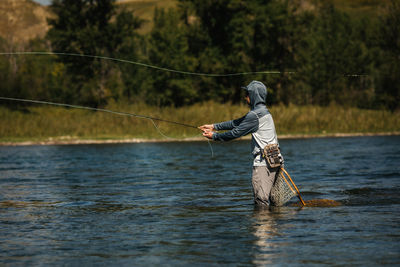 Man fishing in river against trees