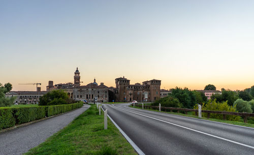 Road amidst buildings against sky during sunset