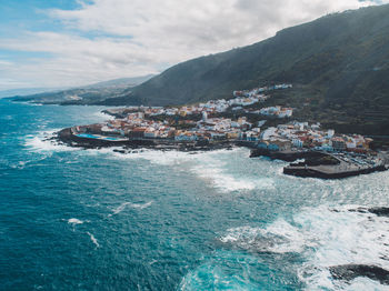 Aerial view of sea by mountains against sky