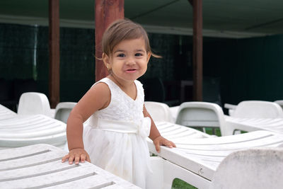 Portrait of smiling girl standing amidst chairs outdoors