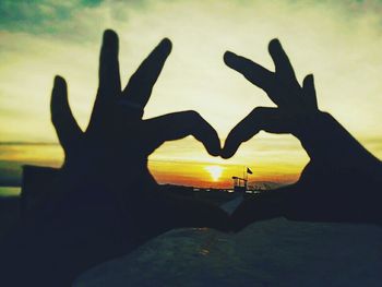 Close-up of hand holding heart shape against sky during sunset