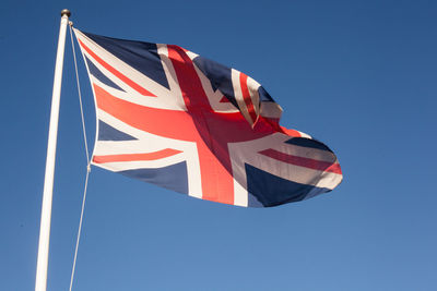 Low angle view of british flag waving against clear blue sky