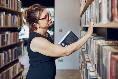 Woman looking for books in public library. teacher searching for literature for reading and learning