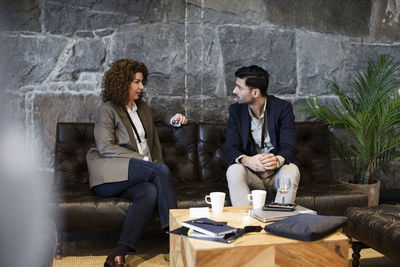 Businesswoman discussing strategy with businessman while sitting on sofa at seminar