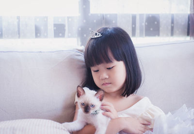 Cute girl with kitten sitting on sofa at home