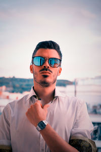 Portrait of young man wearing sunglasses standing against sky