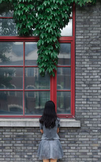 Rear view of woman standing against window of house