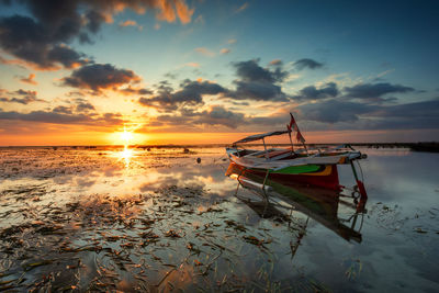 Boat moored at beach against sky during sunset