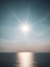 Sun shining over sea against sky