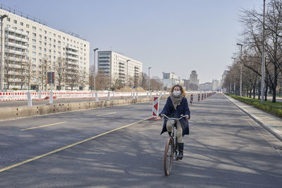 Woman wearing mask riding bicycle on road in city