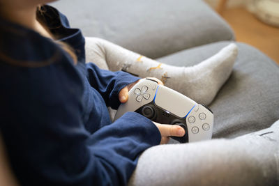 Midsection of girl holding video game remote while sitting on sofa