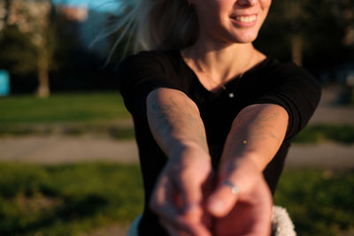 Midsection of young woman gesturing while standing on field