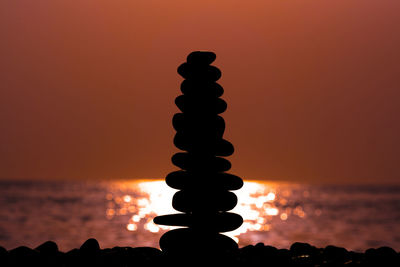 Silhouette rocks by sea against sky during sunset